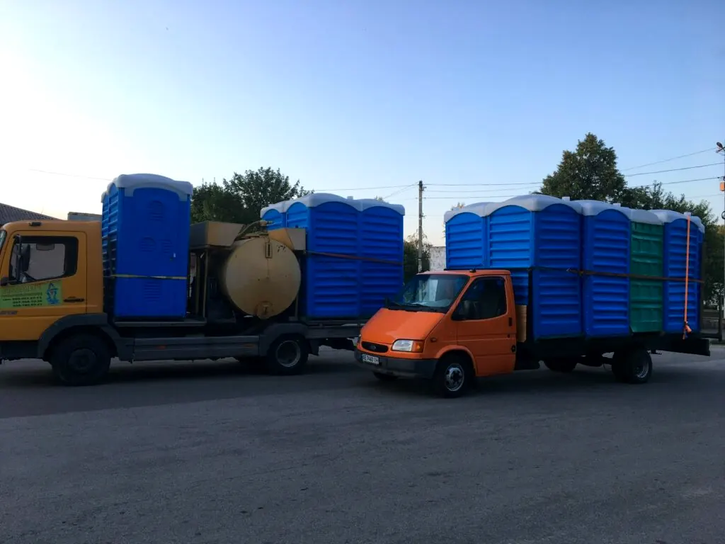 Жовтий ілосос і вантажівка з синіми кабінами біотуалетів